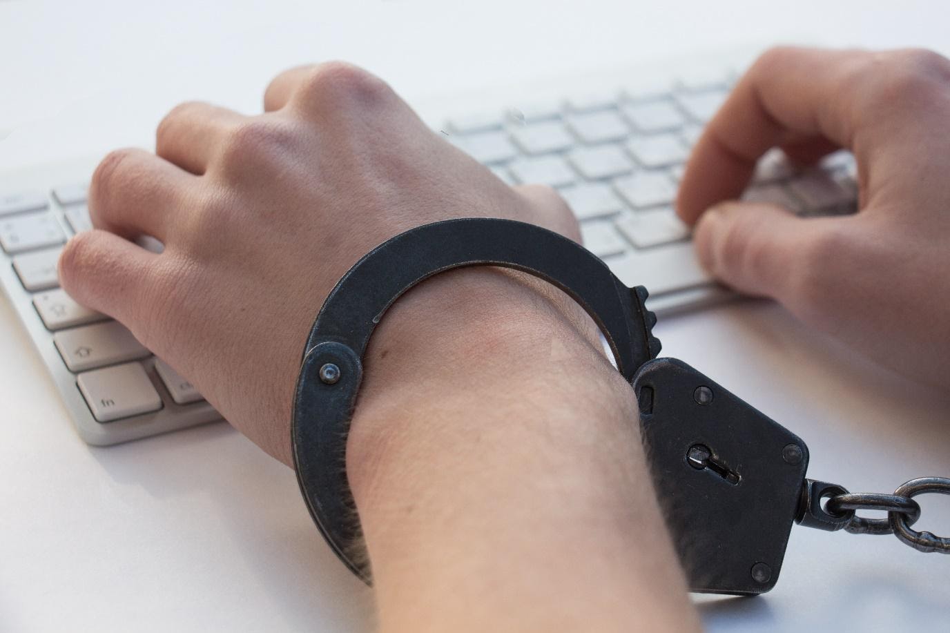 Hände in schwarzen Handschellen auf weißer Tastatur