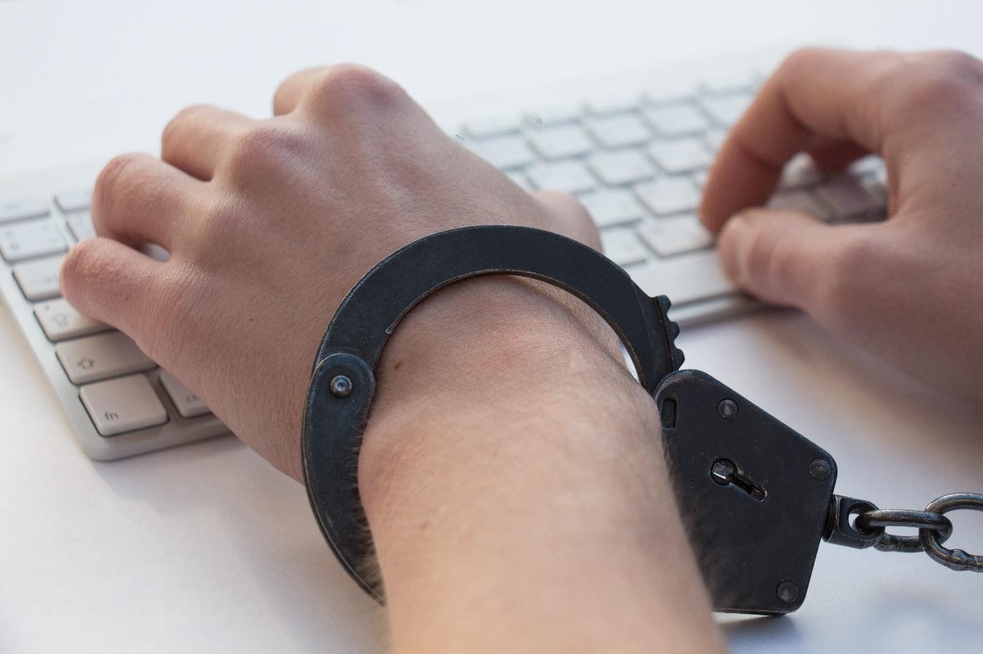 Hände in Handschellen auf weißer Computertastatur