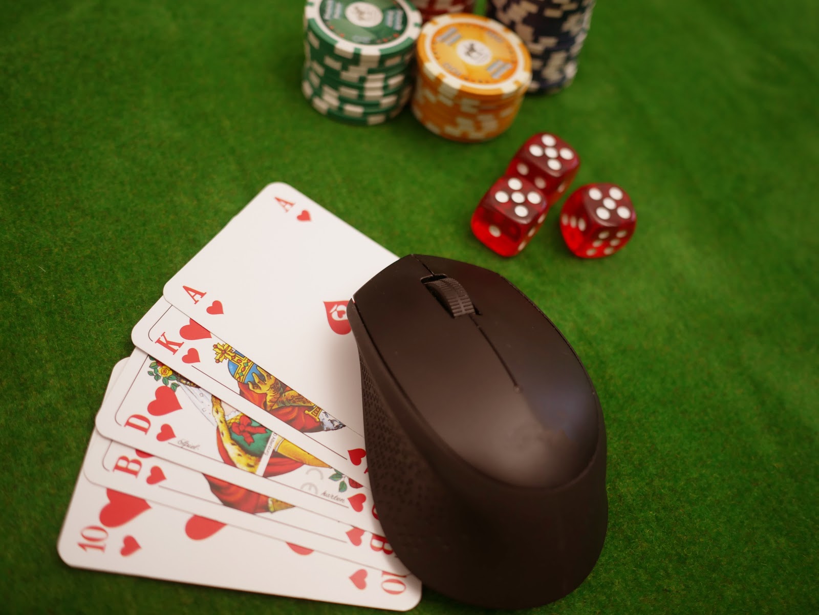 Computermaus, Spielkarten, Pokerchips und Würfel auf grünem Pokertisch